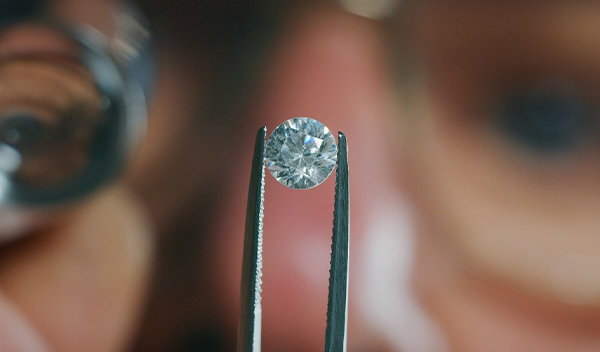 Zlatník drží diamant v pinzete a kontroluje jeho kvalitu